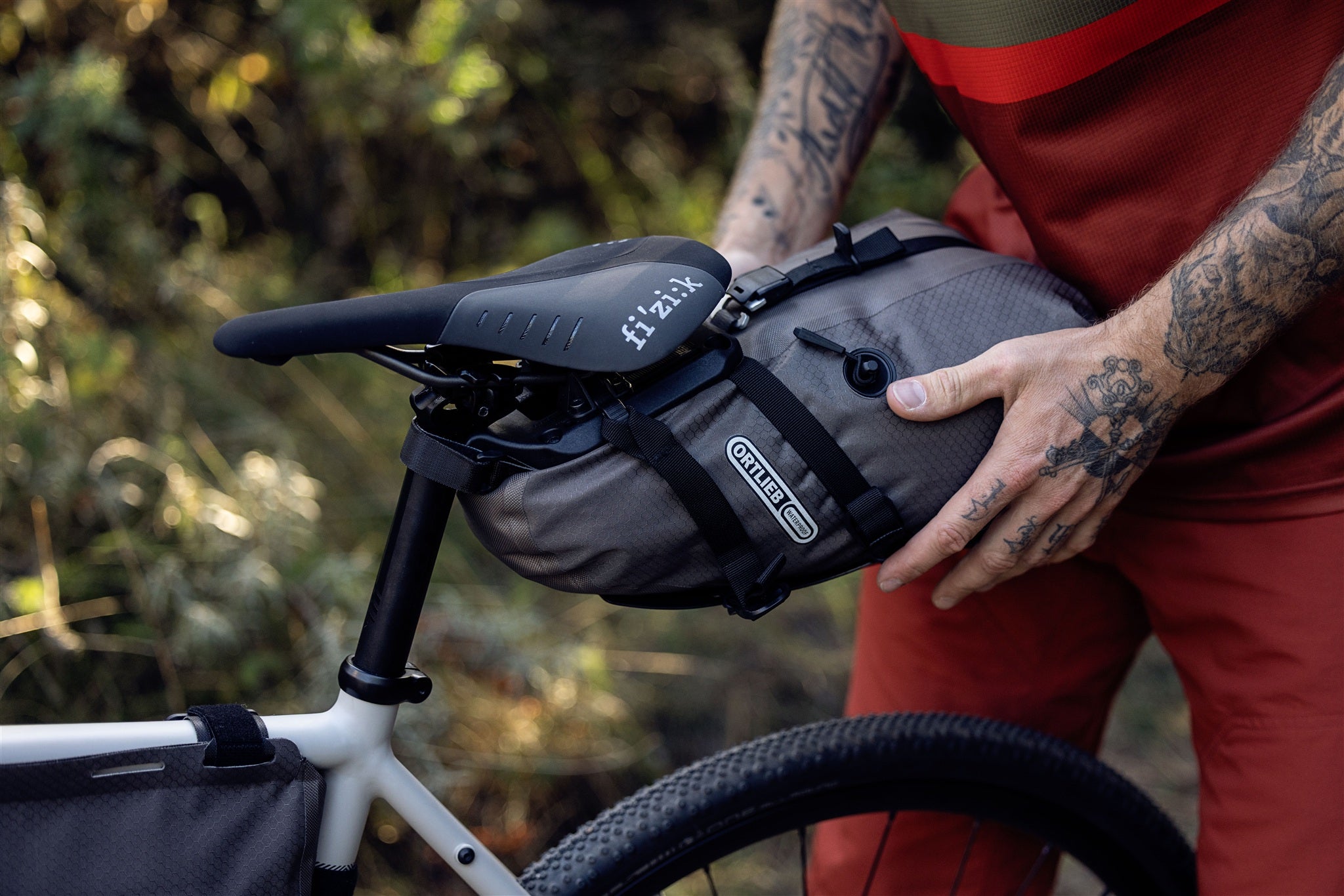 Radfahrer befestigt ORTLIEB Seat-Pack QR in dark-sand am Fahrradsattel im Wald